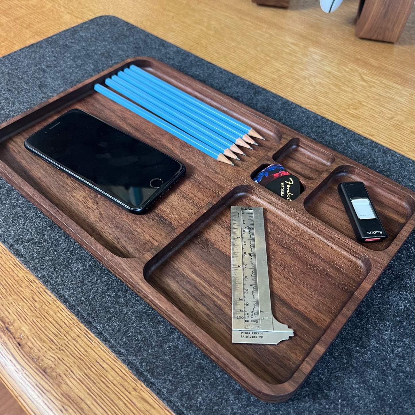 Wooden tray with compartments holding a phone, pencils, a ruler, and other items on a wooden surface.