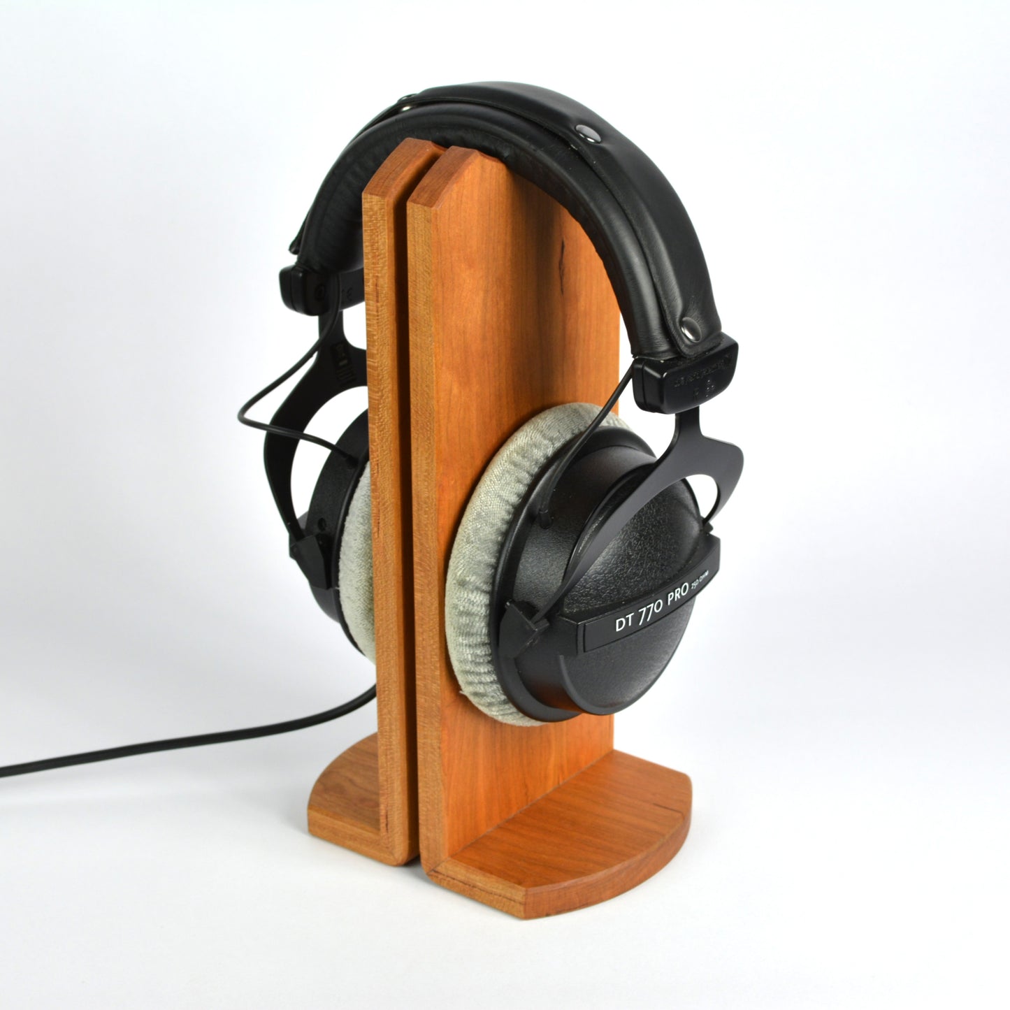 Wooden headphone stand holding a pair of headphones on a white background