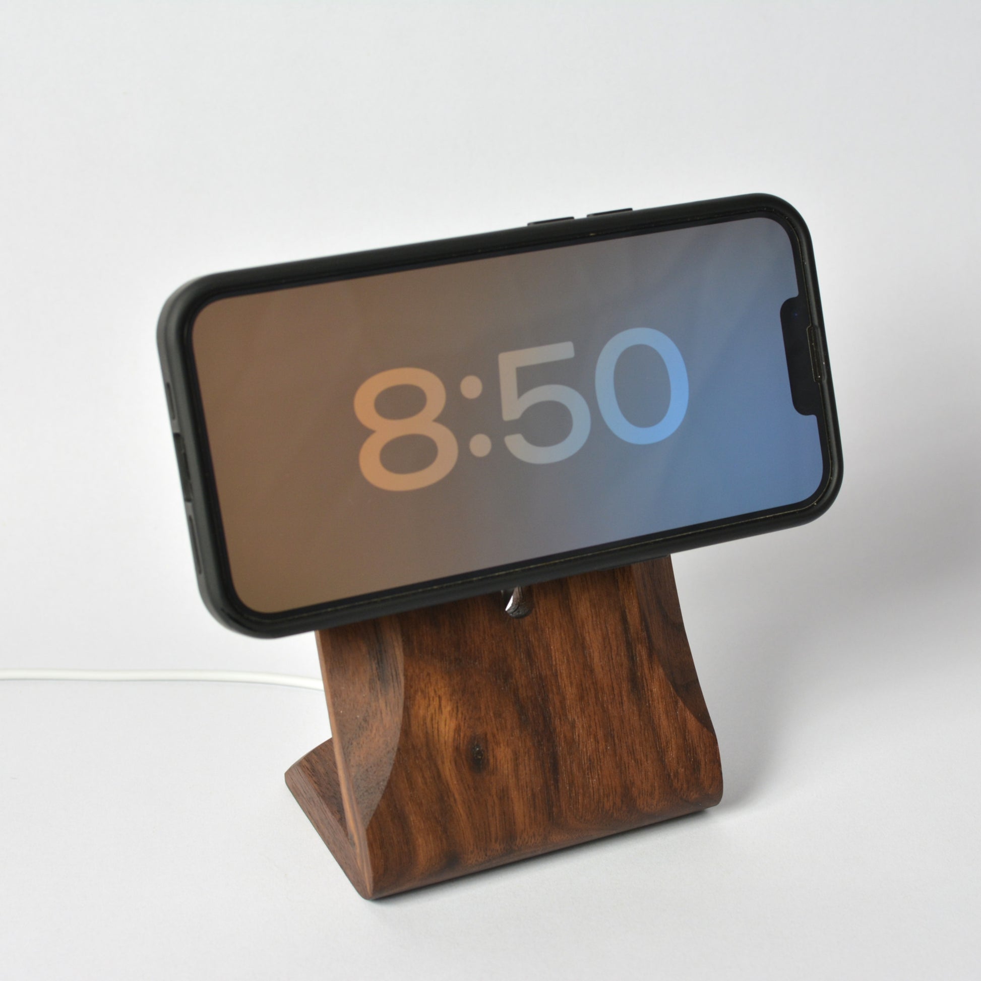 Wooden phone stand holding a smartphone displaying the time on a white background