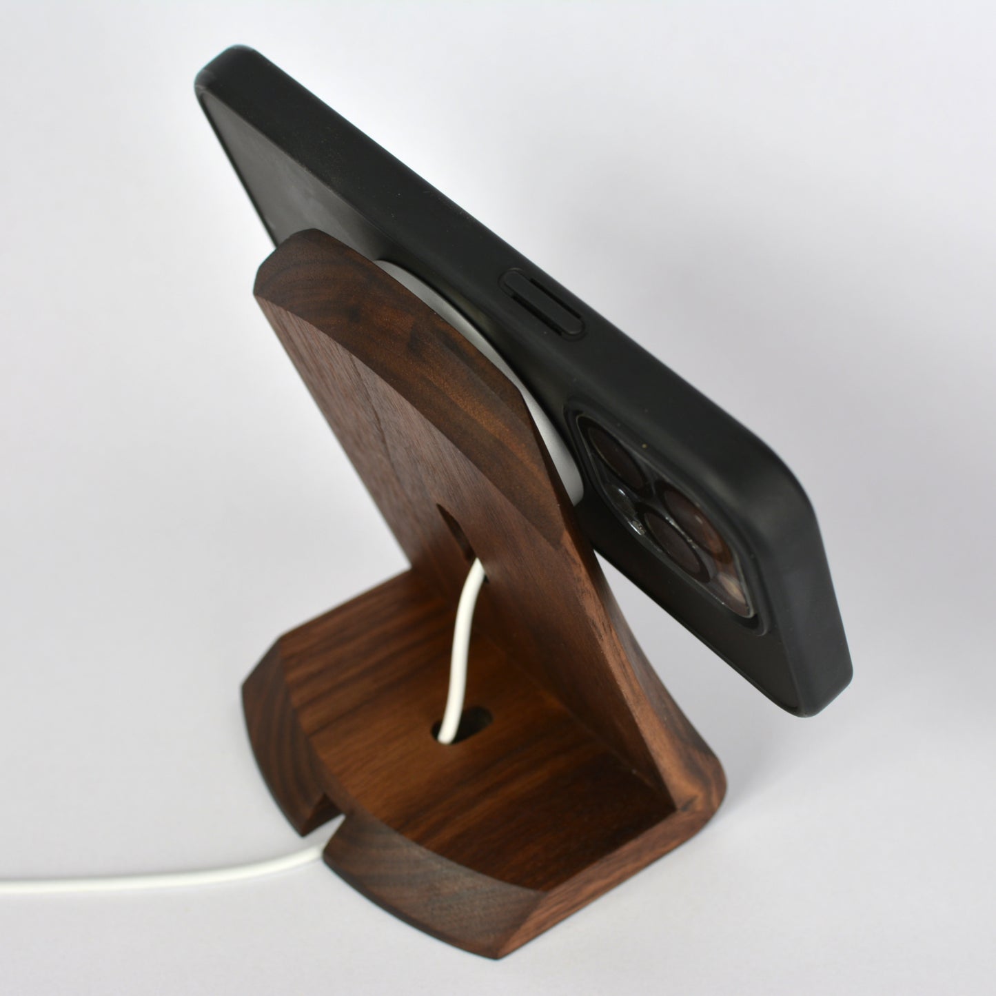 Wooden phone stand holding a black phone on a white background