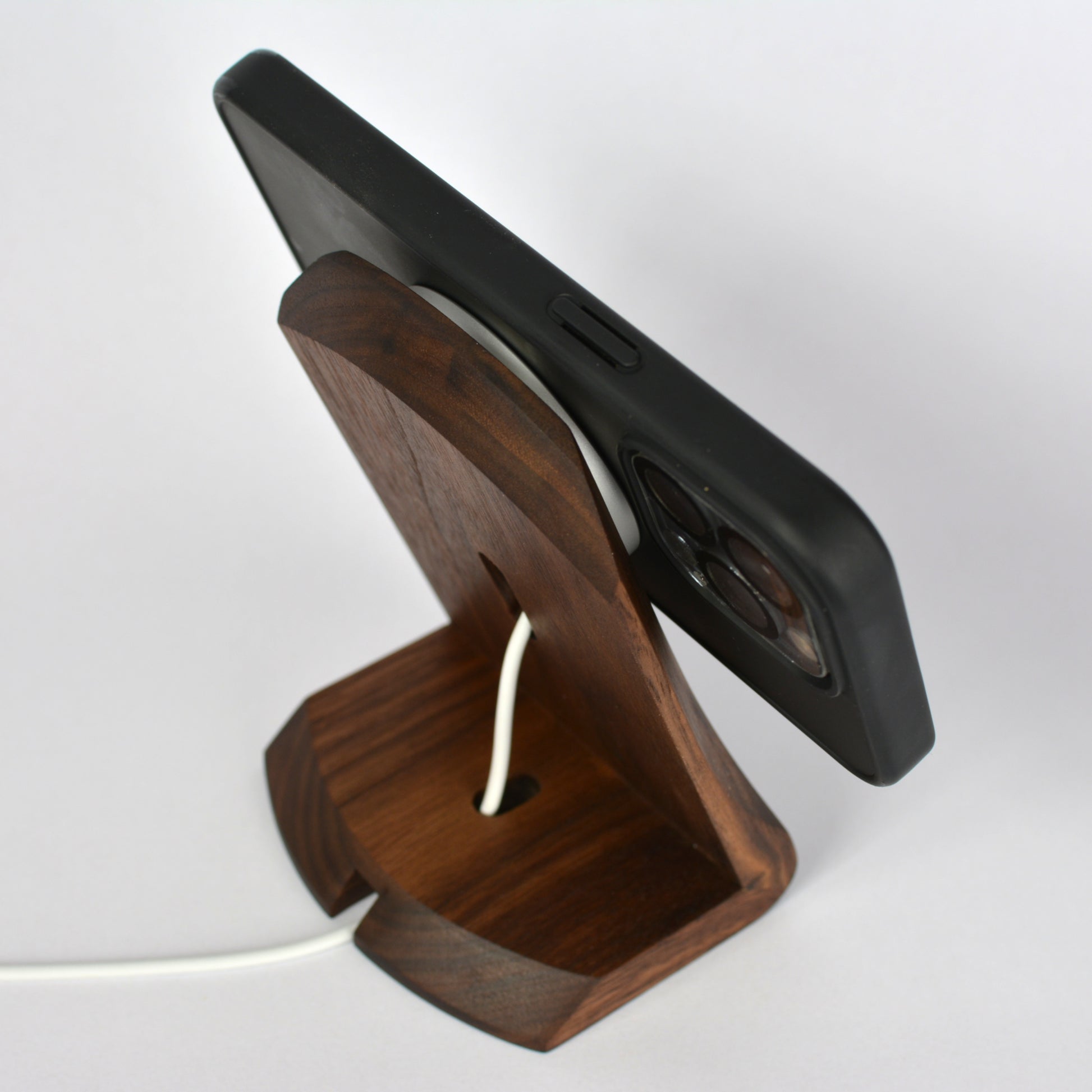 Wooden phone stand holding a black phone on a white background