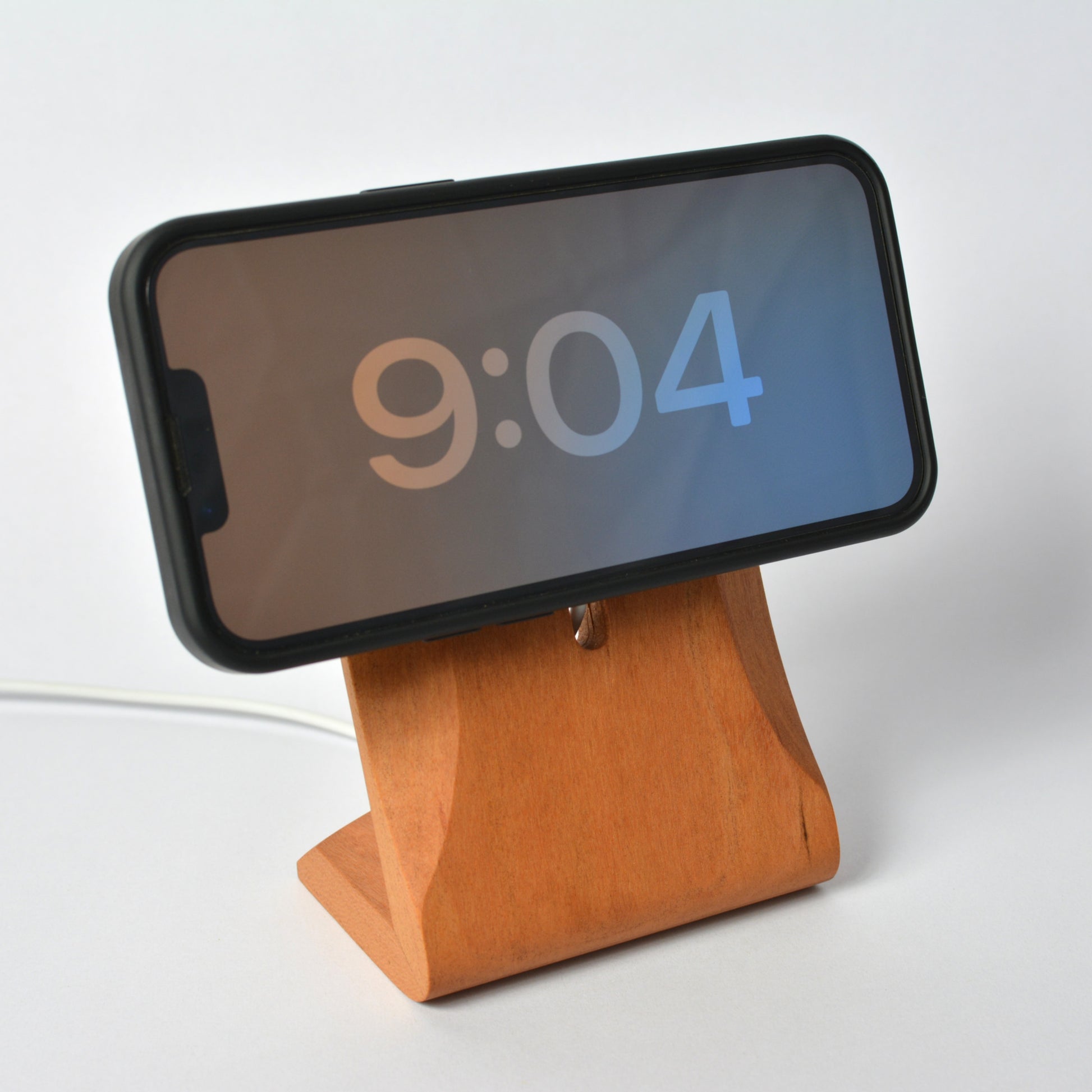 Phone on a wooden stand displaying the time '9:04' on a white background