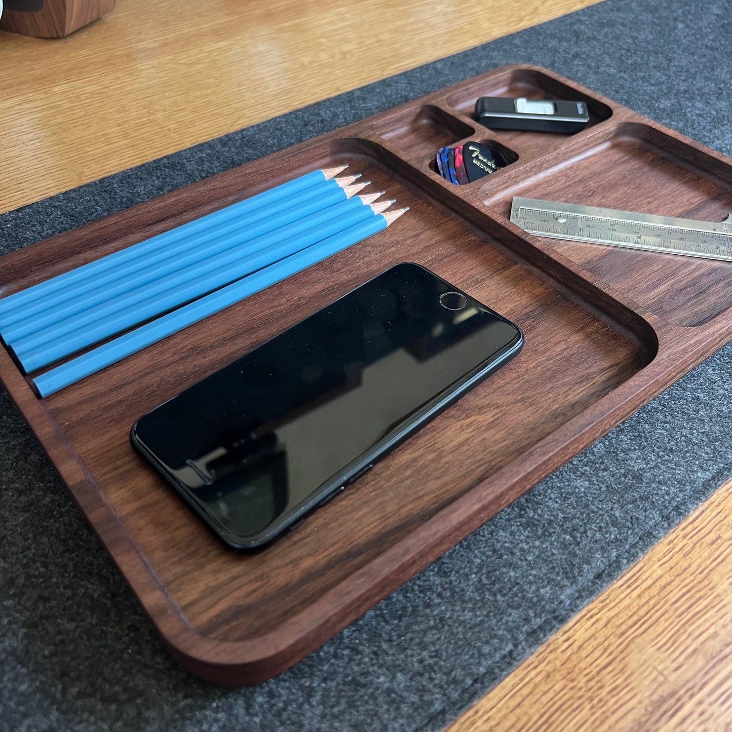 Wooden tray with stationery items including pencils, a phone, and a ruler on a wooden surface.