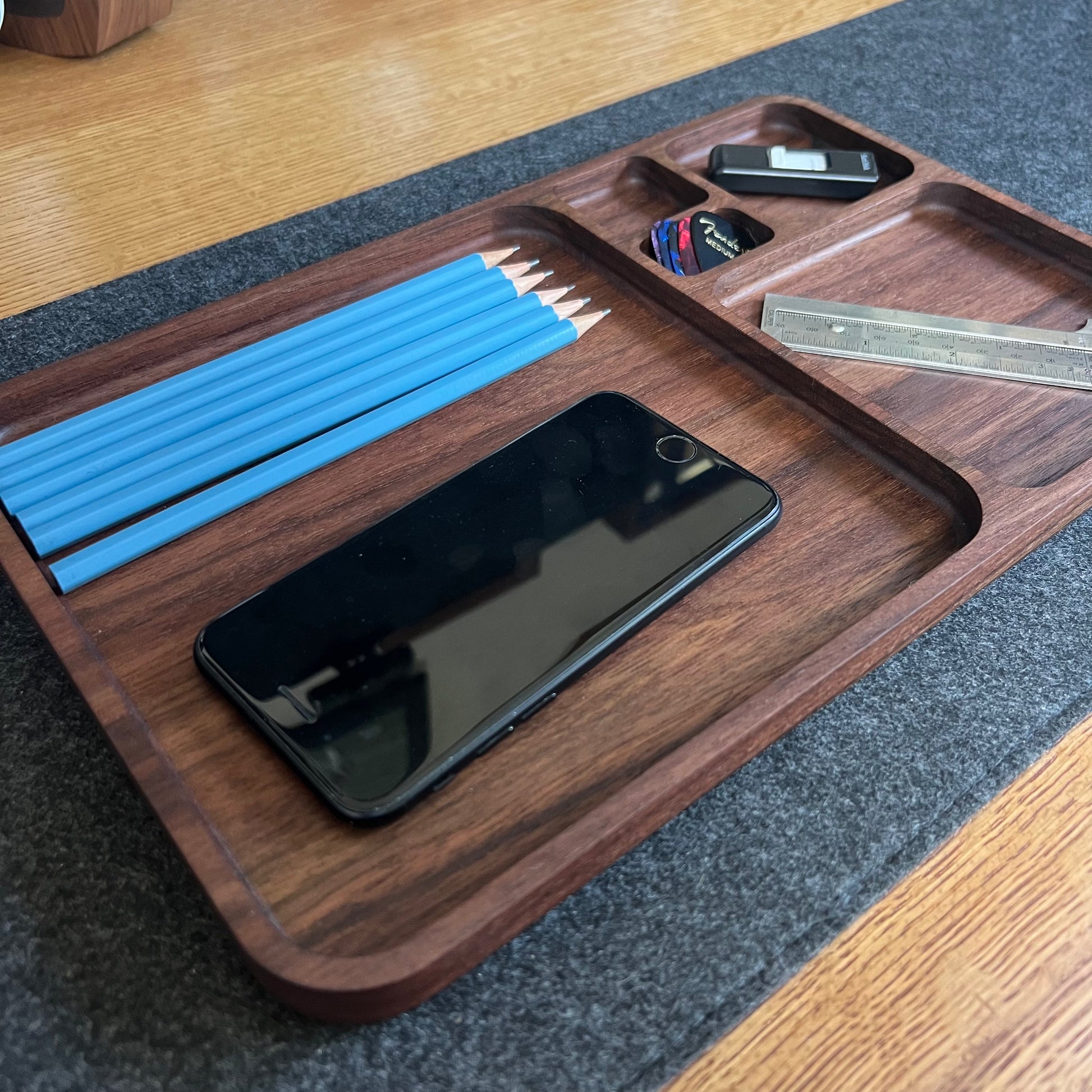 Wooden tray with stationery items including pencils, a phone, and a ruler on a wooden surface.