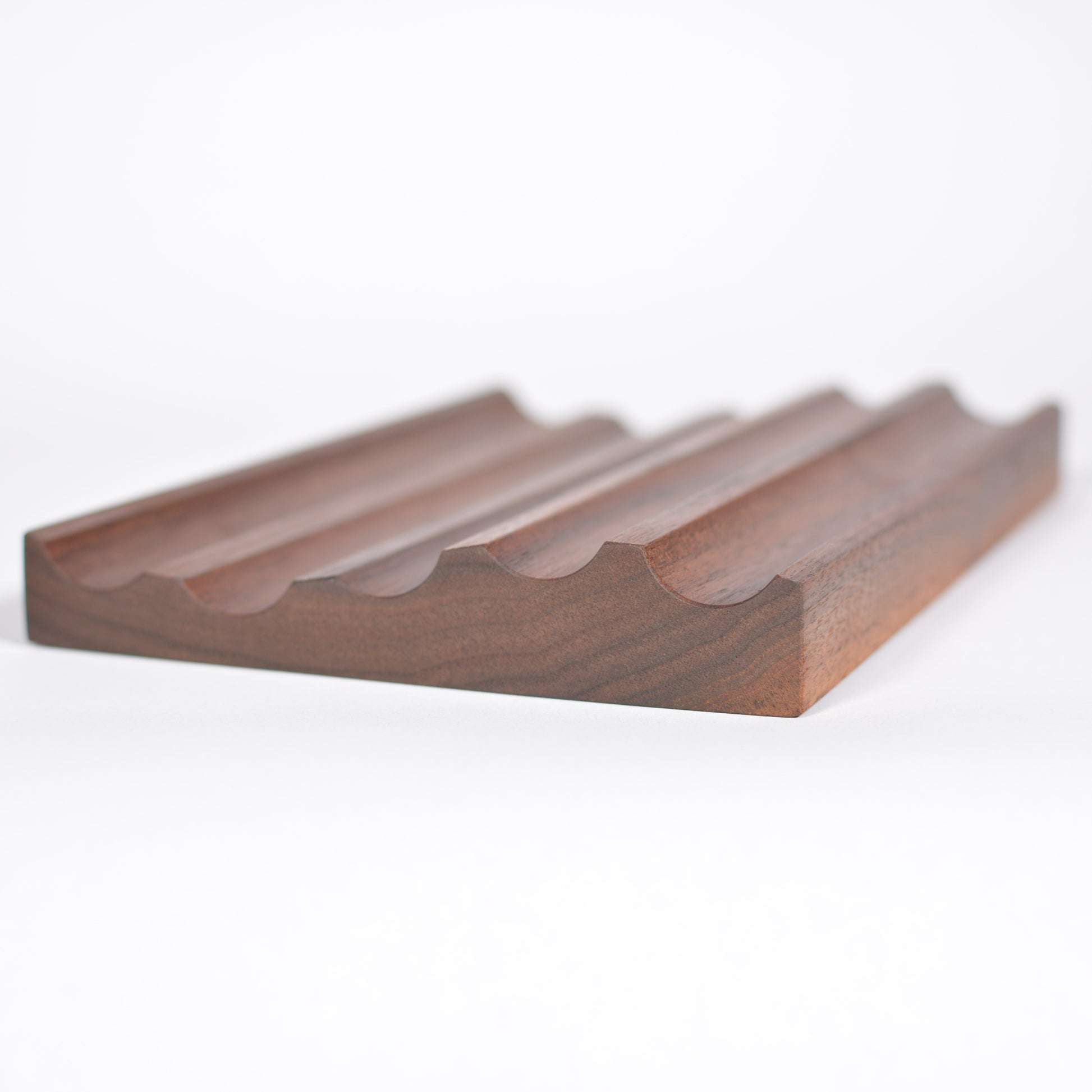 A dark brown wooden tray with a wavy, ribbed pattern, photographed on a clean white background.